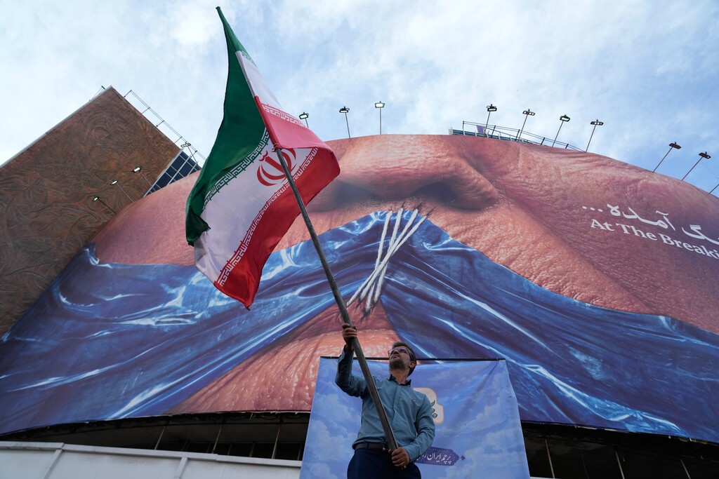 A man waves an Iranian flag for a pro-government campaign under a billboard with graphic showing Strait of Hormuz and sewn lips of U.S. President Donald Trump in a square in downtown Tehran, Wednesday, May 6, 2026. (AP Photo/Vahid Salemi)