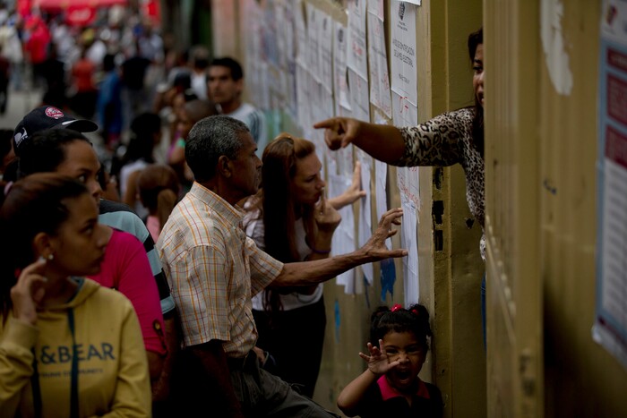 People look for their names on voter registration lists outside a polling station during regional elections in Caracas, Venezuela, Sunday, Oct. 15, 2017. Elections could tilt a majority of the states' 23 governorships back into opposition control for the first time in nearly two decades of socialist party rule, though the government says the newly elected governors will be subordinate to a pro-government assembly. (AP Photo/Fernando Llano)