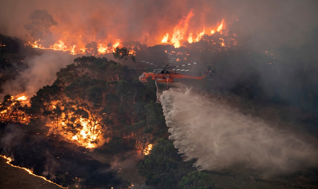 (State Government of Victoria via AP) In this Monday, Dec. 30, 2019 photo provided by State Government of Victoria, a helicopter tackles a wildfire in East Gippsland, Victoria state, Australia. Wildfires burning across Australia's two most-populous states trapped residents of a seaside town in apocalyptic conditions Tuesday, Dec. 31, and were feared to have destroyed many properties and caused fatalities.
