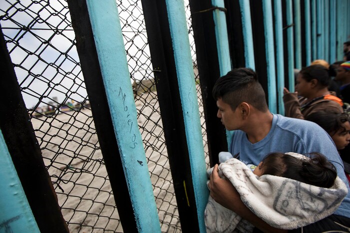 (Hans-Maximo Musielik) | The Associated Press)  A member of the Central American migrant caravan, holding a child, looks through the border wall toward a group of people gathered on the U.S. side, as he stands on the beach where the border wall ends in the ocean, in Tijuana, Mexico, Sunday, April 29, 2018. U.S. immigration lawyers are telling Central Americans in a caravan of asylum-seekers that traveled through Mexico to the border with San Diego that they face possible separation from their children and detention for many months. They say they want to prepare them for the worst possible outcome.