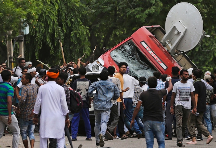 Dera Sacha Sauda sect members overturn an OB van on the streets of Panchkula, India, Friday, Aug. 25, 2017. Deadly riots have broken out in a north Indian town after a court convicted their guru, who calls himself Saint Dr. Gurmeet Ram Rahim Singh Ji Insaan, of raping two of his followers. Mobs also attacked journalists and set fire to government buildings and railway stations. (AP Photo/Altaf Qadri)