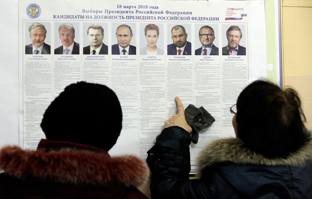 Women examine a poster of candidates inside a polling station during presidential elections in St.Petersburg, Russia, Sunday, March 18, 2018. Russians are voting in a presidential election in which Vladimir Putin is seeking a fourth term in the Kremlin. (AP Photo/Dmitri Lovetsky)