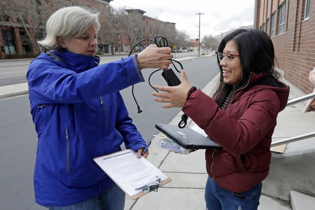 (Rick Bowmer  |  AP file photo) English teacher Valerie Gates, left, distributes a computer to help with remote learning, to West Hight School junior Monserrat Roque at West High School Thursday, March 19, 2020, in Salt Lake City. Utah students in public elementary, middle and high schools will not take year-end standardized tests this spring because of the coronavirus pandemic that has shuttered schools for at least two weeks, the state board of education decided Thursday.