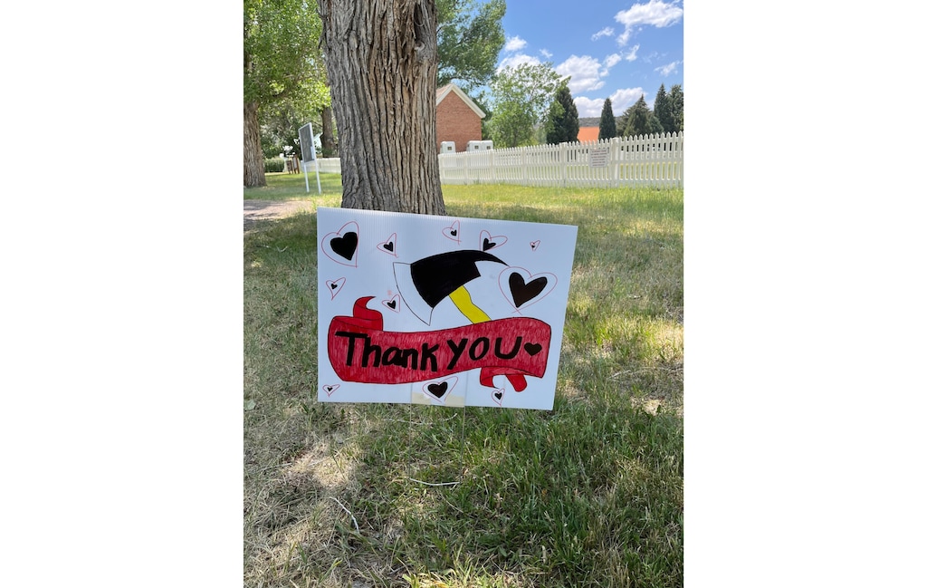 A yard sign with an image of a fire axe, a red ribbon that says, "Thank You," and black hearts decorates a yard in Pine Valley.