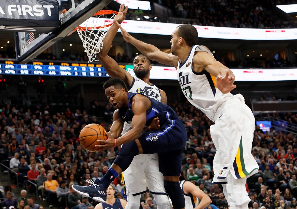 Dallas Mavericks' Yogi Ferrell, bottom, is defended by Utah Jazz's Derrick Favors, top left, and Rudy Gobert, right, as he attempts a basket in the first half of an NBA basketball game on Saturday, Feb. 24, 2018, in Salt Lake City. (AP Photo/Kim Raff)