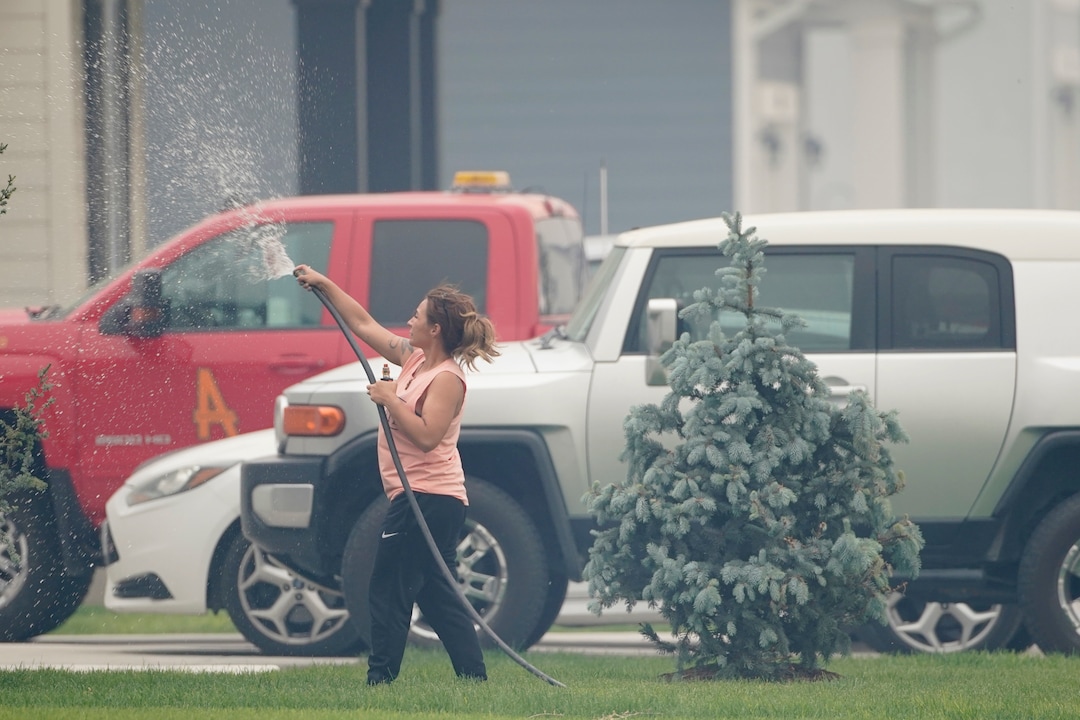 (George Frey  |  for The Salt Lake Tribune) A woman sprays her house a hose in south Saratoga Springs due to a nearby wildfire on June 28, 2020.