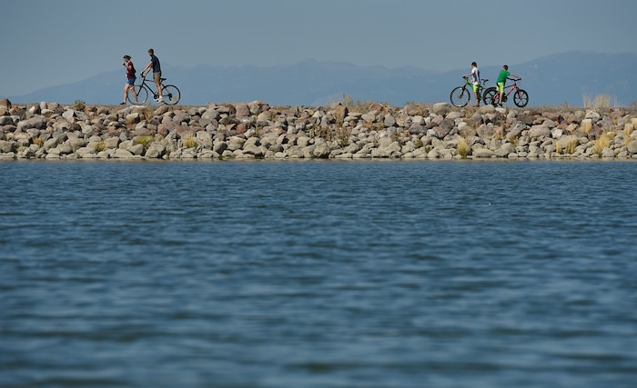 (Francisco Kjolseth  |  The Salt Lake Tribune)  Kids ride their bikes around the popular Black Ridge Reservoir in Herriman on Tuesday, Aug. 28, 2018, where warning signs have been posted after an outbreak of algae-related toxin cyanobacteria was detected in the water.