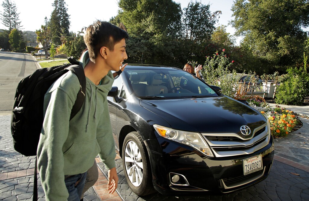 (Ben Margot | The Associated Press) In this photo taken Tuesday, Oct. 29, 2019, Zum driver Stacey Patrick, right, waves goodbye to student Saahas Kohli, left, and his mother, Alpa Kohli, obscured behind her son, as he returns home from school in Saratoga, Calif. A handful of ride-hailing companies have surfaced that allow parents to order rides, and in some cases childcare, for children using smartphone apps. The promise is alluring at a time when children are expected to accomplish a dizzying array of extracurricular activities and the boundaries between work and home have blurred. But the companies face hurdles convincing parents that a stranger hired by a ride-hailing company is trustworthy enough to ferry their most precious passengers.