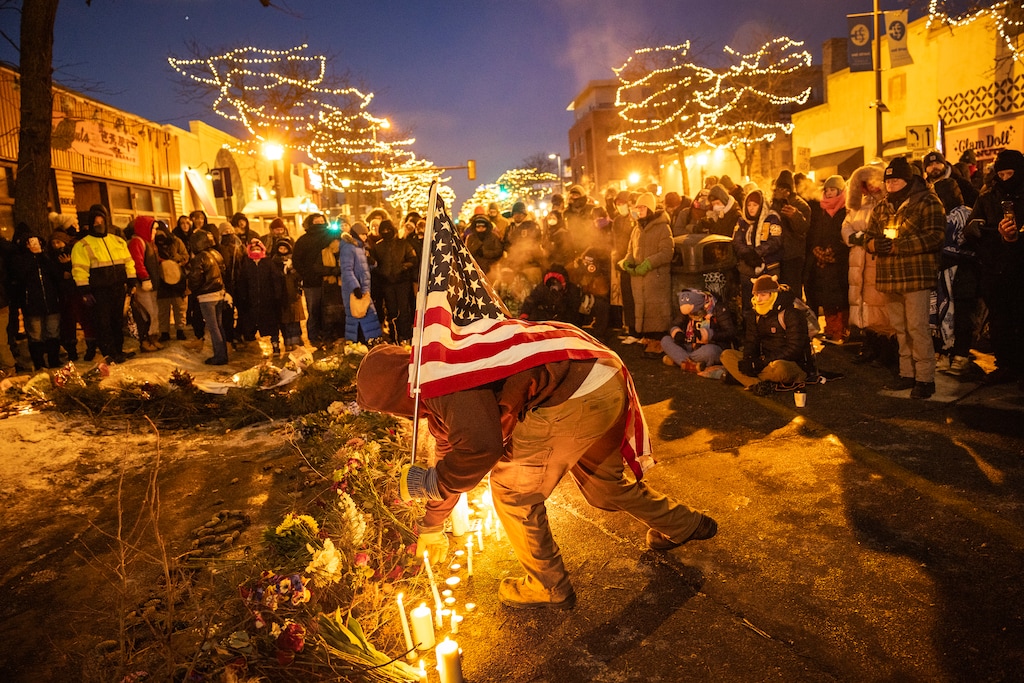 (David Guttenfelder | The New York Times) A man carrying an American flag visits a makeshift memorial at the site where Alex Pretti was shot and killed in Minneapolis.