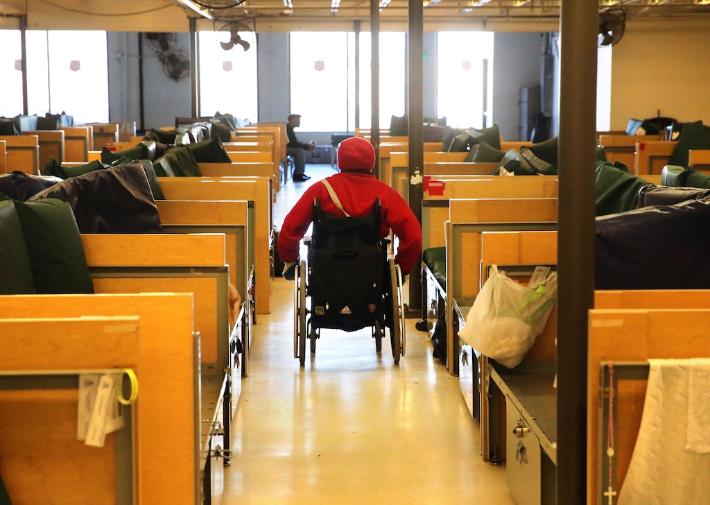 In this Nov. 26, 2014 photo, A homeless man with multiple sclerosis rolls past a row of beds inside the Salvation Army shelter in Denver. (AP Photo/Brennan Linsley)