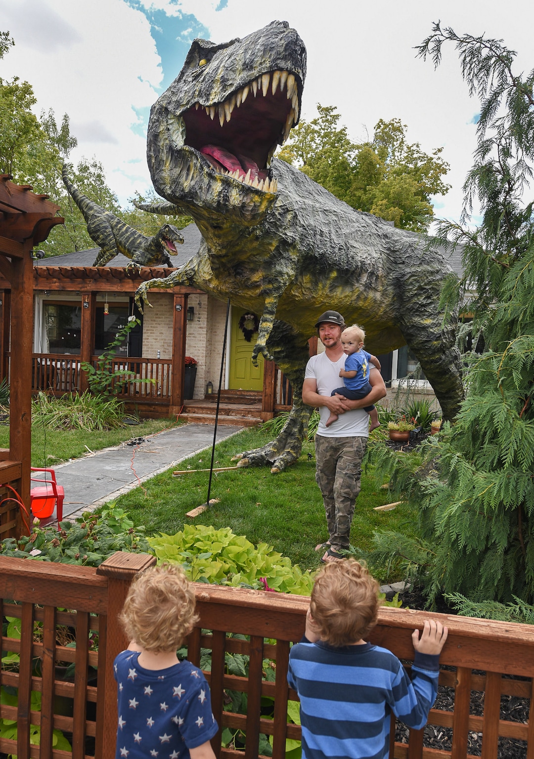(Francisco Kjolseth  |  The Salt Lake Tribune)  Young fans check in on the Halloween installation by Ammon Smith, holding his nephew Lincoln Smith, 1,  at 1542 S. 900 East in Salt Lake City after constructing a "maturing adult"-size T. rex along with a pair of velociraptors and pterodactyls. The part-time stay-at-home dad, who made a giant King Kong last year, started construction back in August as he assembled recycled wood, chicken wire, foam, aluminum foil and spray paint for the 12-by-32-foot Jurassic centerpiece and companion pieces.