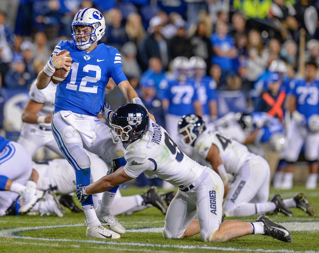 Leah Hogsten  |  The Salt Lake Tribune  Brigham Young Cougars quarterback Tanner Mangum (12) barely slips away from Utah State Aggies linebacker David Woodward (9). Utah State University defeated BYU 45-20 at Lavell Edwards Stadium in Provo, Friday, Oct. 5, 2018.