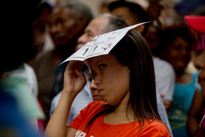 A woman shades her face with voting instructions as she waits in line outside a polling station to cast her ballot during regional elections in Caracas, Venezuela, Sunday, Oct. 15, 2017. Elections could tilt a majority of the states' 23 governorships back into opposition control for the first time in nearly two decades of socialist party rule, though the government says the newly elected governors will be subordinate to a pro-government assembly. (AP Photo/Fernando Llano)