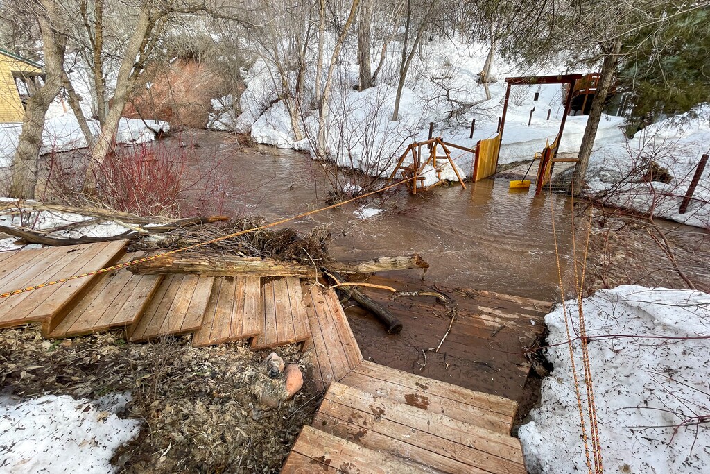 (Trent Nelson | The Salt Lake Tribune) La gente trabaja para salvar una casa mientras Emigration Creek se eleva en Emigration Canyon el miércoles 12 de abril de 2023. Mientras los funcionarios públicos han instado a los habitantes de Utah a prepararse para las inundaciones mediante la compra de pólizas de seguro, es posible que miles no tengan acceso y pocas comunidades participen en un programa federal para hacerlo más asequible.