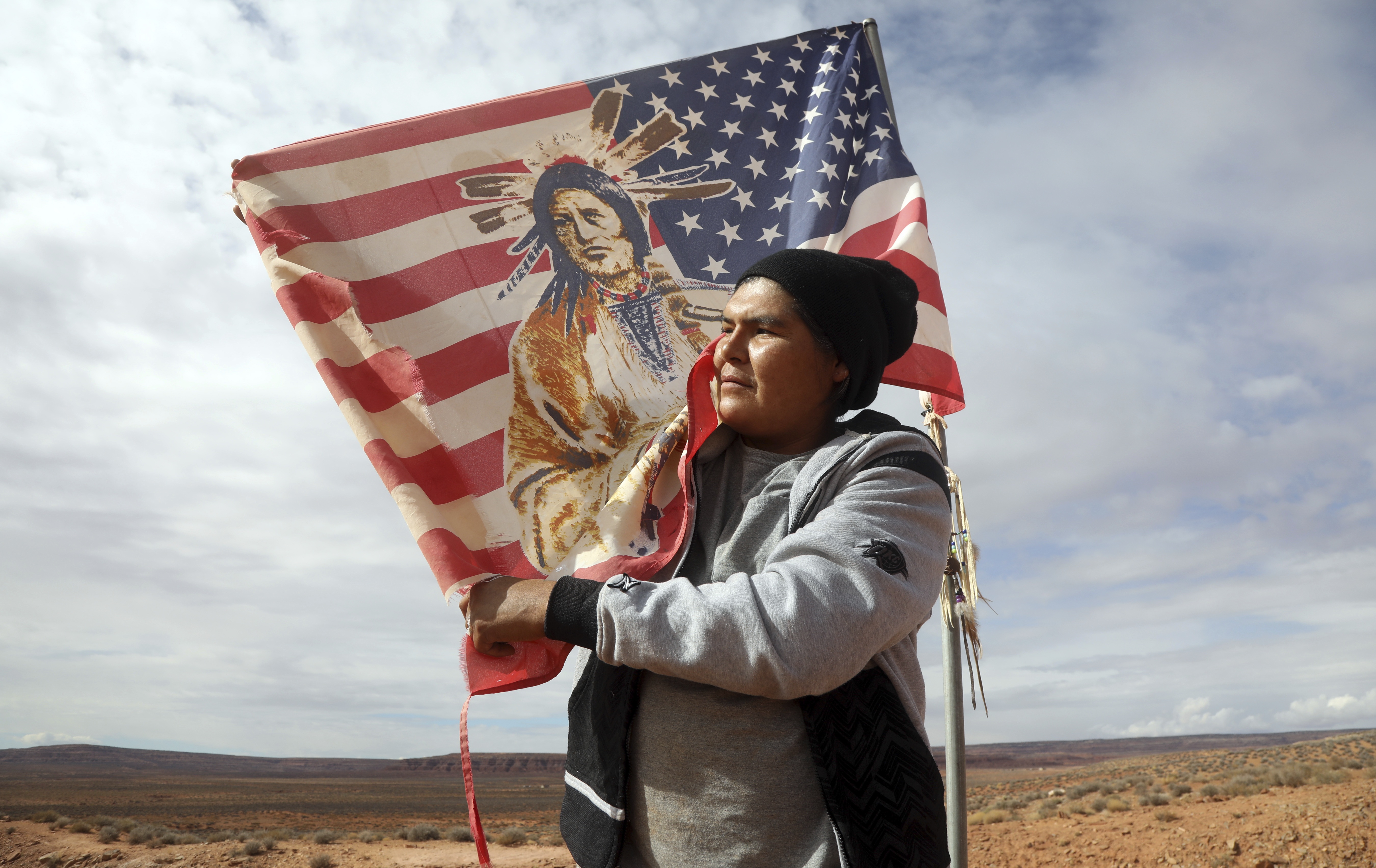 (Rick Bowmer  |  AP Photo)  In this Thursday, Oct. 25, 2018, photo, Brandon Nez displays his flag near his jewelry stand in Monument Valley, Utah, where tourists stand the highway to recreate a famous running scene from the movie "Forest Gump.". As Native American tribes around the country fight for increased access to the ballot box, Navajo voters in one Utah county could tip the balance of power in the first general election since a federal judge ordered overturned their voting districts as illegally drawn to minimize native voices.