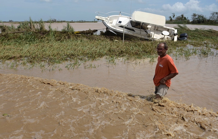 A man wades through a flooded road, past a boat, in the Toa Ville community two days after the impact of Hurricane Maria in Toa Baja, Puerto Rico, Friday, Sept. 22, 2017. Because of flooding, thousands of people are being evacuated from Toa Baja after the municipal government opened the gates of the Rio La Plata Dam. (AP Photo/Carlos Giusti)