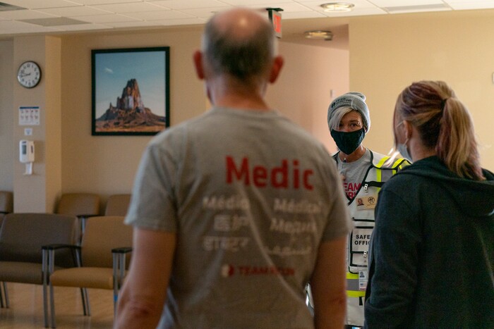 Christra McDermont, a U.S. Navy veteran from Los Angeles, center, talks with other Team Rubicon volunteers, Dr. Stan Chartoff, with the U.S. Air Force Reserve from Hartford Conn., left, and EMT Tracy Thomas from Omaha, Neb., in a patient waiting area at the Kayenta Health Center on the Navajo reservation in Kayenta, Ariz., on April 19, 2020. The reservation has some of the highest rates of coronavirus in the country. Team Rubicon is helping with medical operations as cases of COVID-19 surge. (AP Photo/Carolyn Kaster)