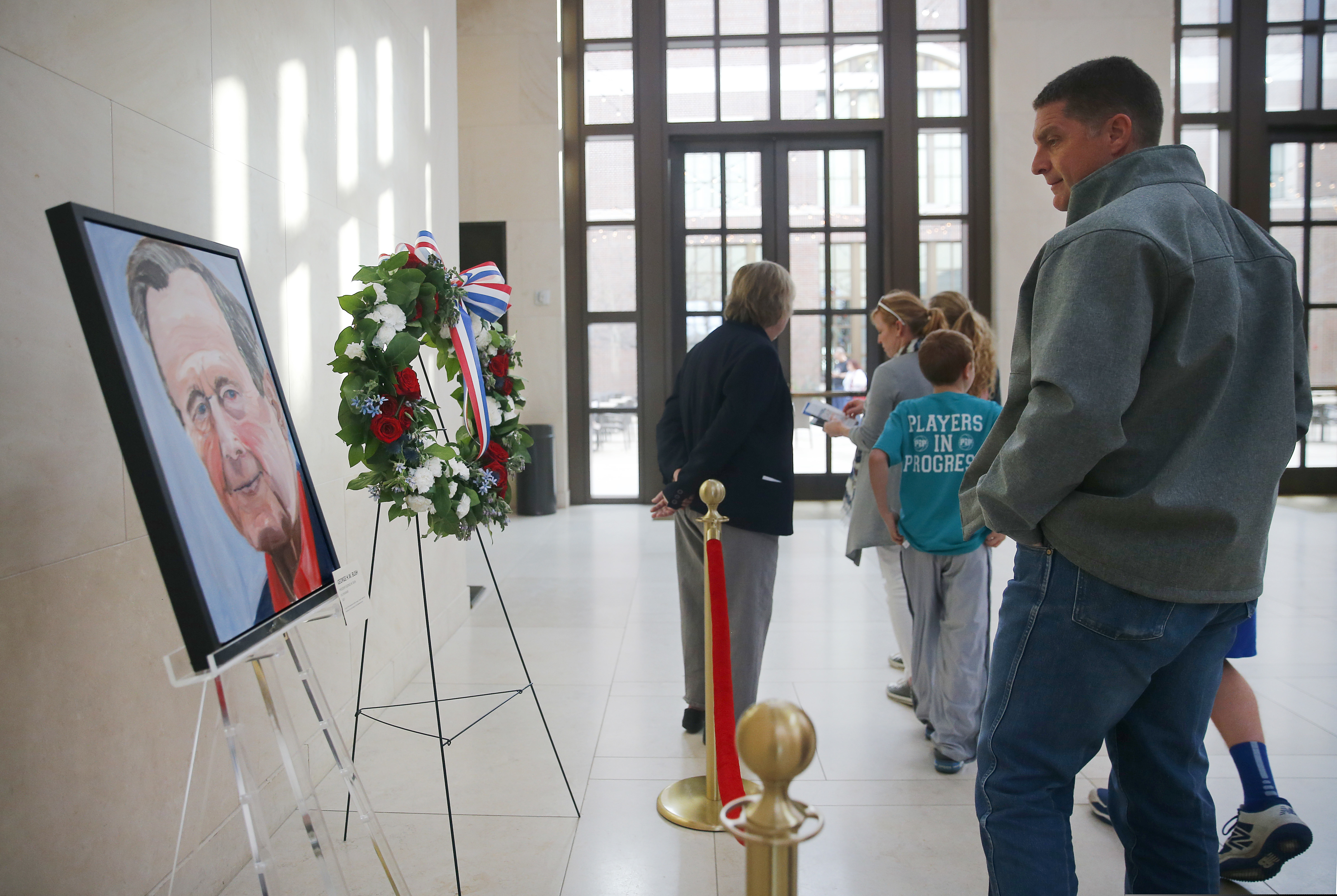Scott Fowler of Van Alstyne, Texas and his family pass by a painted portrait of the late 41st President George H.W. Bush -- painted by his son, Pres. George W. Bush -- in the atrium area of the younger Bush's George W. Bush Presidential Library and Museum in University Park, Texas, Sunday, Dec. 2, 2018. President George H.W. Bush died last week in Maine. The painting was done by his son and former 43rd President George W. Bush. The elder Bush will be laid to rest next to his wife Barbara at the George H.W. Bush Library Center in College Station, Texas this week. (Tom Fox/The Dallas Morning News via AP)