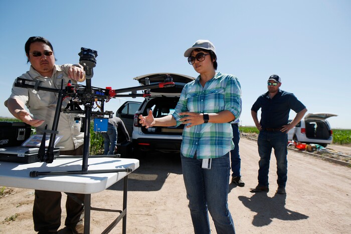 (David Zalubowski | AP Photo) In this Thursday, July 11, 2019, photograph, United States Department of Agriculture Kevin Yemoto, left, an engineering technician, joins Huihui Zhang in setting up a drone for flight over a research farm northeast of Greeley, Colo. as Kendall DeJonge, also of the USDA, looks on. Researchers are using drones carrying imaging cameras over the fields in conjunction with stationary sensors connected to the internet to chart the growth of crops in an effort to integrate new technology into the age-old skill of farming.