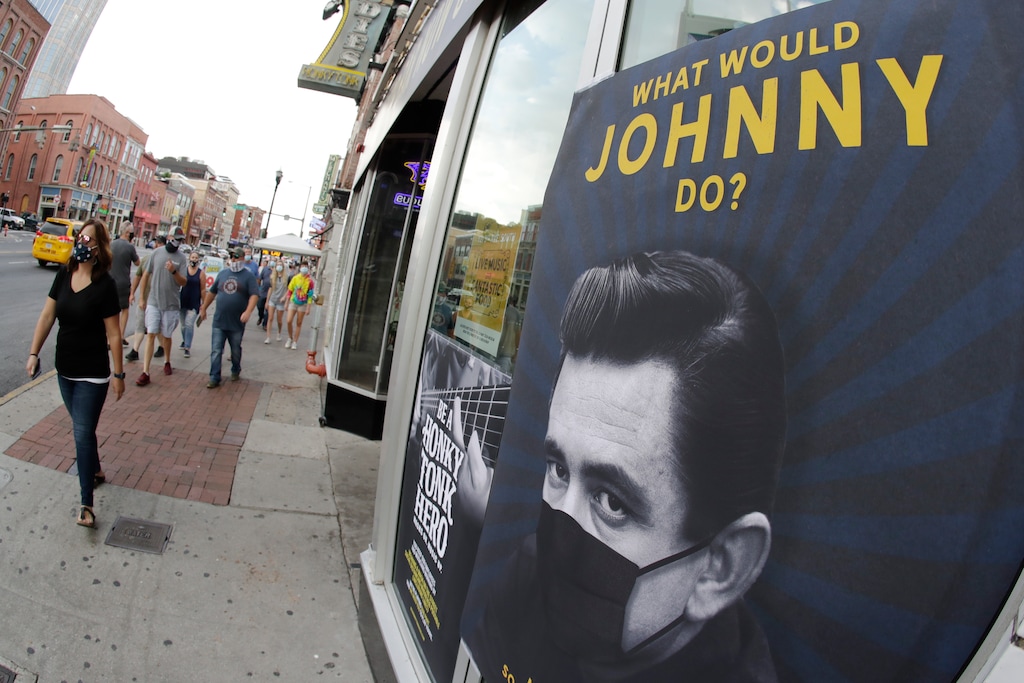 A poster showing country music legend Johnny Cash wearing a mask is attached to a storefront Wednesday, Aug. 5, 2020, in Nashville, Tenn. The wearing of face coverings is required in most public indoor and outdoor situations in Nashville due to an increase of COVID-19 cases. (AP Photo/Mark Humphrey)