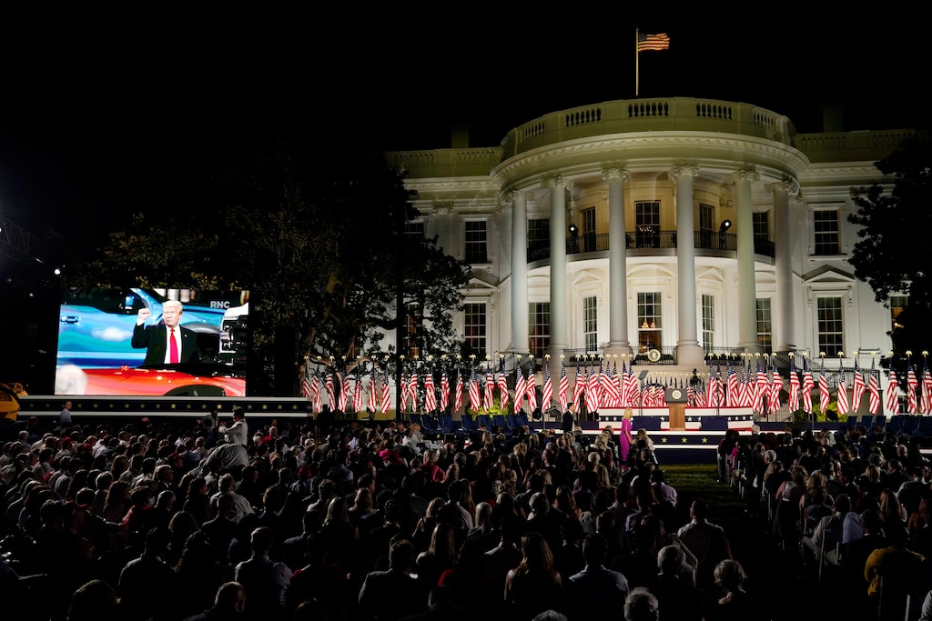 (Evan Vucci | AP file photo)  People watch video screens before President Donald Trump speaks from the South Lawn of the White House on the fourth day of the Republican National Convention, Thursday, Aug. 27, 2020, in Washington.