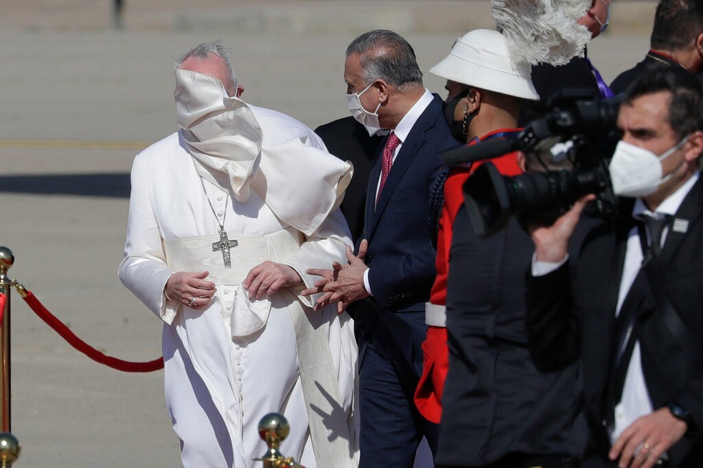 (Andrew Medichini | AP) A gust of wind blows Pope Francis's mantle as he stands by Iraqi Prime Minister Mustafa al-Kadhimi upon his arrival at Baghdad's international airport, Iraq, Friday, March 5, 2021. Pope Francis heads to Iraq on Friday to urge the country's dwindling number of Christians to stay put and help rebuild the country after years of war and persecution, brushing aside the coronavirus pandemic and security concerns.