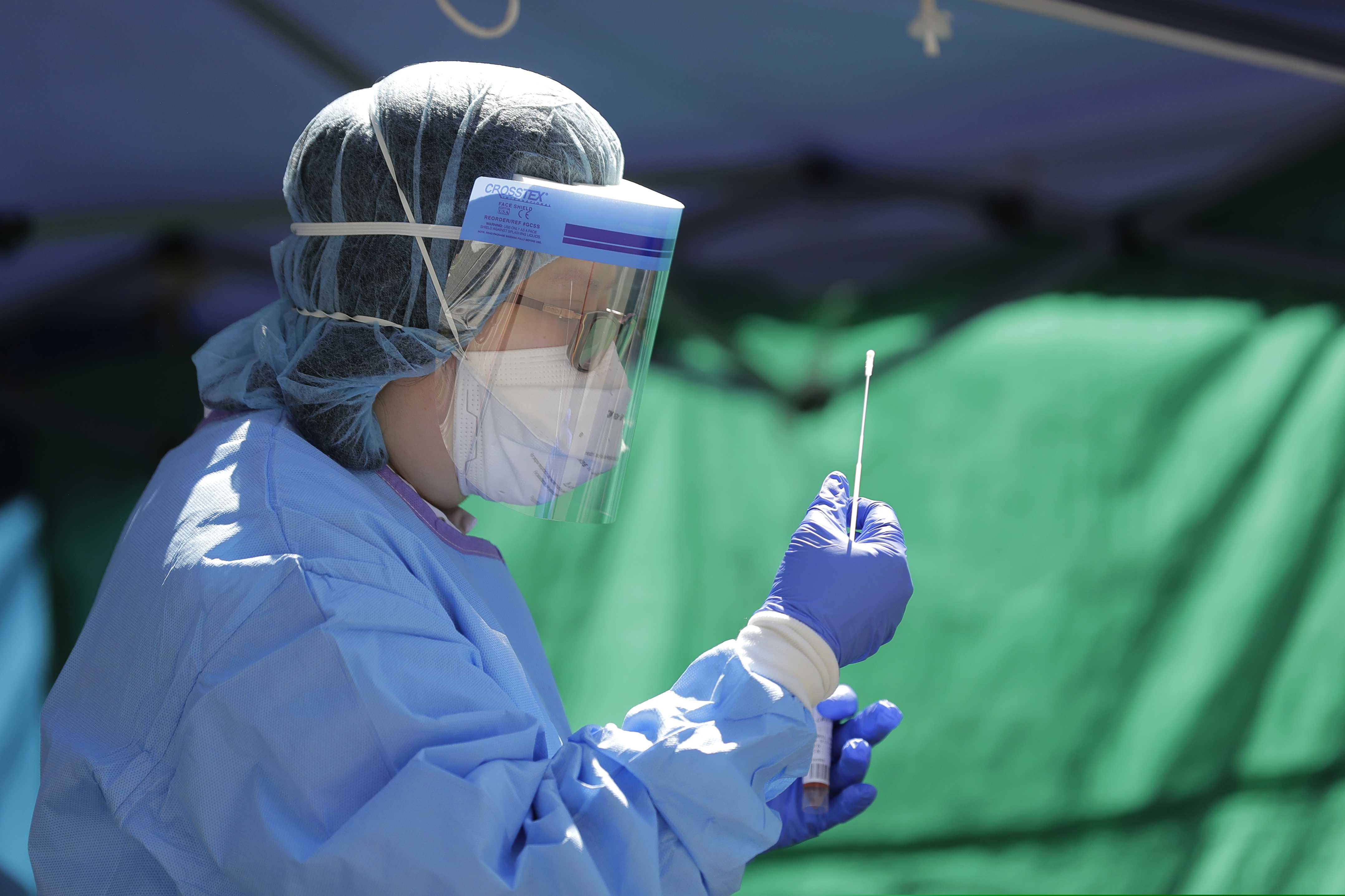 (Ted S. Warren | AP file photo) Tina Nguyen, a nurse at at the International Community Health Services clinic in Seattle's International District, examines a nose swab while conducting walk- and drive-up testing for COVID-19, Friday, May 15, 2020.