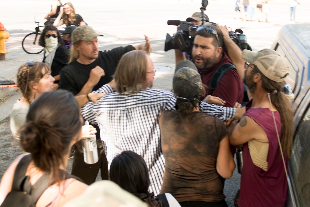 (Jeremy Harmon |  The Salt Lake Tribune) A man in a black and white shirt tries to keep people from attacking a news photographer following an inland port protest on Tuesday, July 9, 2019.