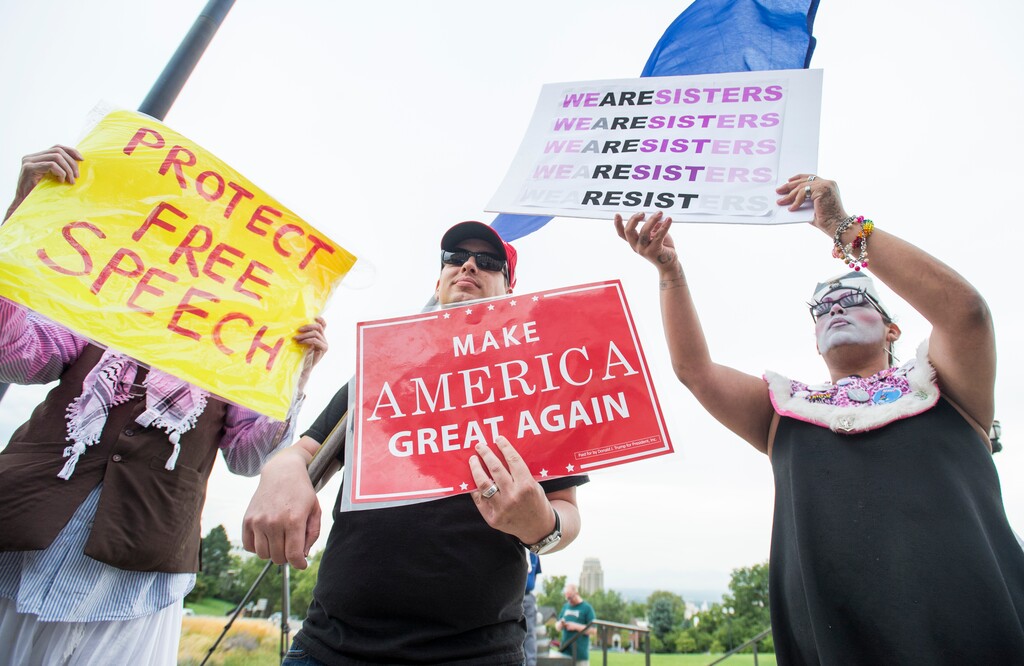 (Rick Egan  |  The Salt Lake Tribune)   Mia  Willie Anderson hides behind his sign, next to an unnamed Trump supporter and  Sister Foster Chiiild, as they jockey for space at the "One Utah" Rally for Unity at the State Capitol on Monday, August 14, 2017.