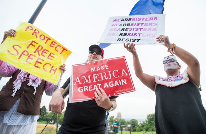 (Rick Egan  |  The Salt Lake Tribune)   Mia  Willie Anderson hides behind his sign, next to an un-named Trump supporter and  Sister Foster Chiiild, as the jocky for space at the "One Utah" Rally for Unity at the State Capitol, Monday, August 14, 2017.


