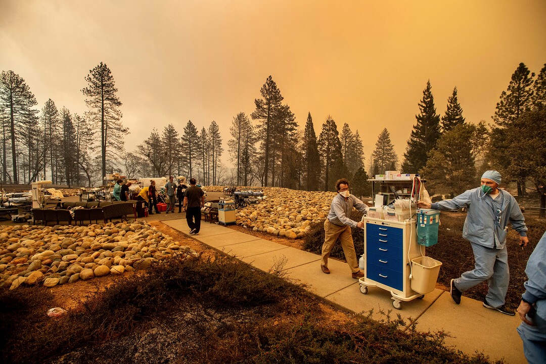 Medical workers move equipment from a makeshift emergency room while the Feather River Hospital burns as the Camp Fire rages through Paradise, Calif., on Thursday, Nov. 8, 2018. Tens of thousands of people fled a fast-moving wildfire Thursday in Northern California, some clutching babies and pets as they abandoned vehicles and struck out on foot ahead of the flames that forced the evacuation of an entire town. (AP Photo/Noah Berger)