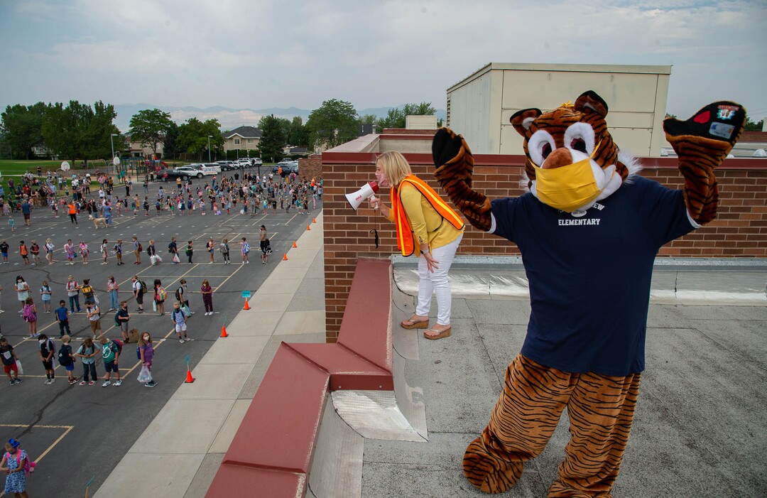 (Francisco Kjolseth  |  The Salt Lake Tribune)  Home of the Cubs, Canyon View Elementary school mascot Bennie, played by PTA president Emily Weigel waves to kids as school principal Kierstin Draper uses a megaphone to greet students back from the roof of the school. It was the first day of classes for the Canyons School District on Monday, August 24, 2020.