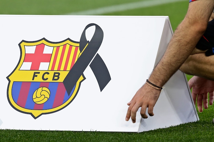 An official places an advertising board with a black ribbon next to the team crest before Barcelona and Betis players observed a minute of silence for the victims of the van attacks before a La Liga soccer match between Barcelona and Betis at the Camp Nou stadium in Barcelona, Spain, Sunday, Aug. 20, 2017. Security was stepped up for the match after a terror attack that killed 14 people and wounded over 120 in Barcelona and police put up scores of roadblocks across northeast Spain on Sunday in hopes of capturing a fugitive suspect at large following the vehicle attack. (AP Photo/Manu Fernandez)