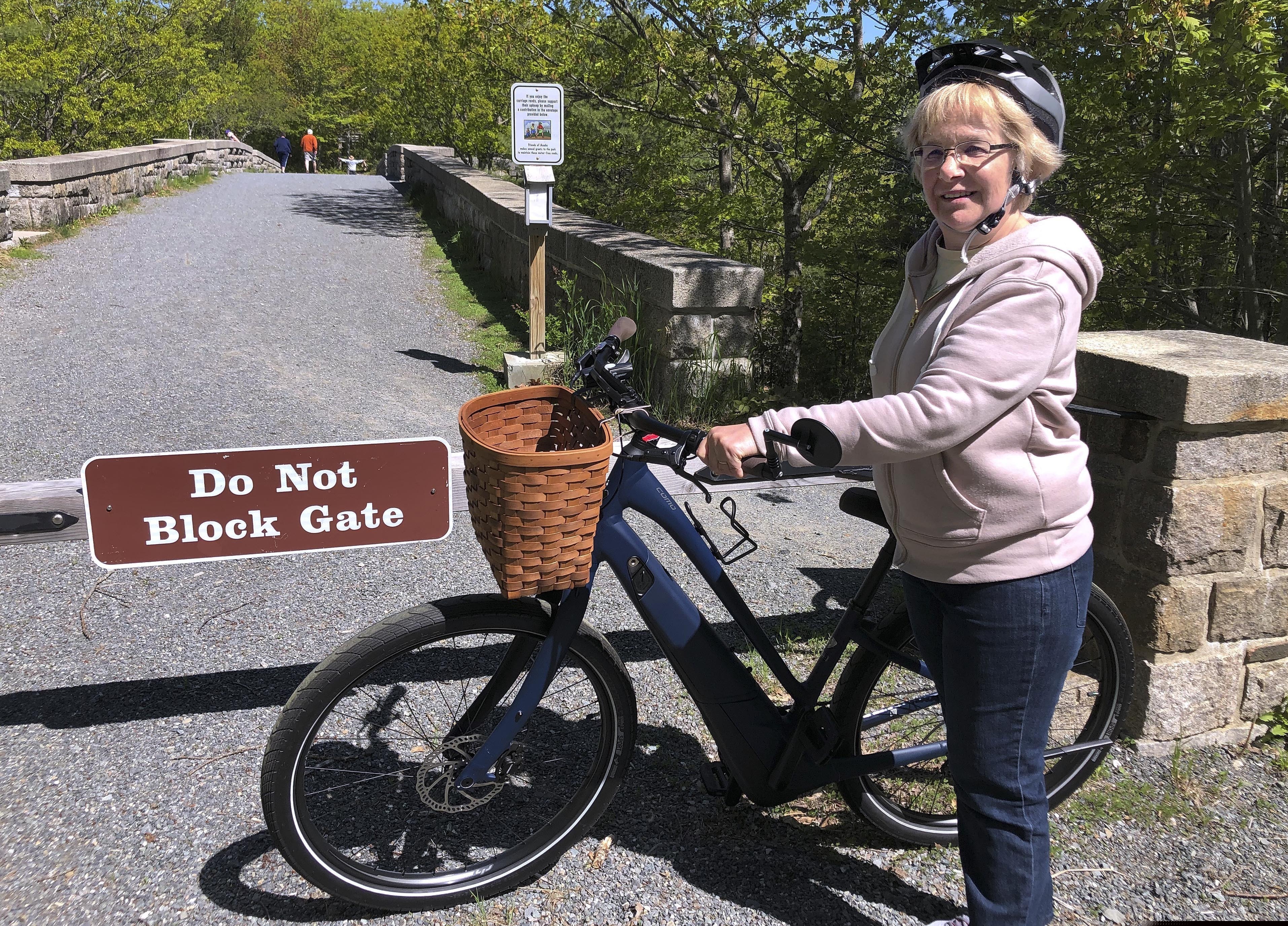 (David Sharp | AP Photo) Janice Goodwin stands by her electric-assist bicycle at a gate near the start of the carriage path system where bikes such as her are banned inside Acadia National Park, June 8, 2018, in Bar Harbor, Maine. Interior Secretary David Bernhardt signed the order on Thursday allowing motorized electric bicycles into national parks and other public lands.