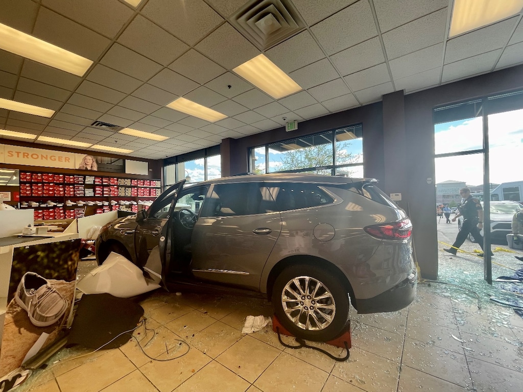 (SLCPD) A Buick Enclave crashed into a Famous Footwear in The Commons shopping center in Sugar House on the afternoon of Saturday, July 2, 2022, trapping a woman underneath it and injuring two others who were in the store — a woman who is 21 weeks pregnant and her 7-year-old daughter. Police believe the woman, 81, who was driving the SUV mistook the gas pedal for the brake.