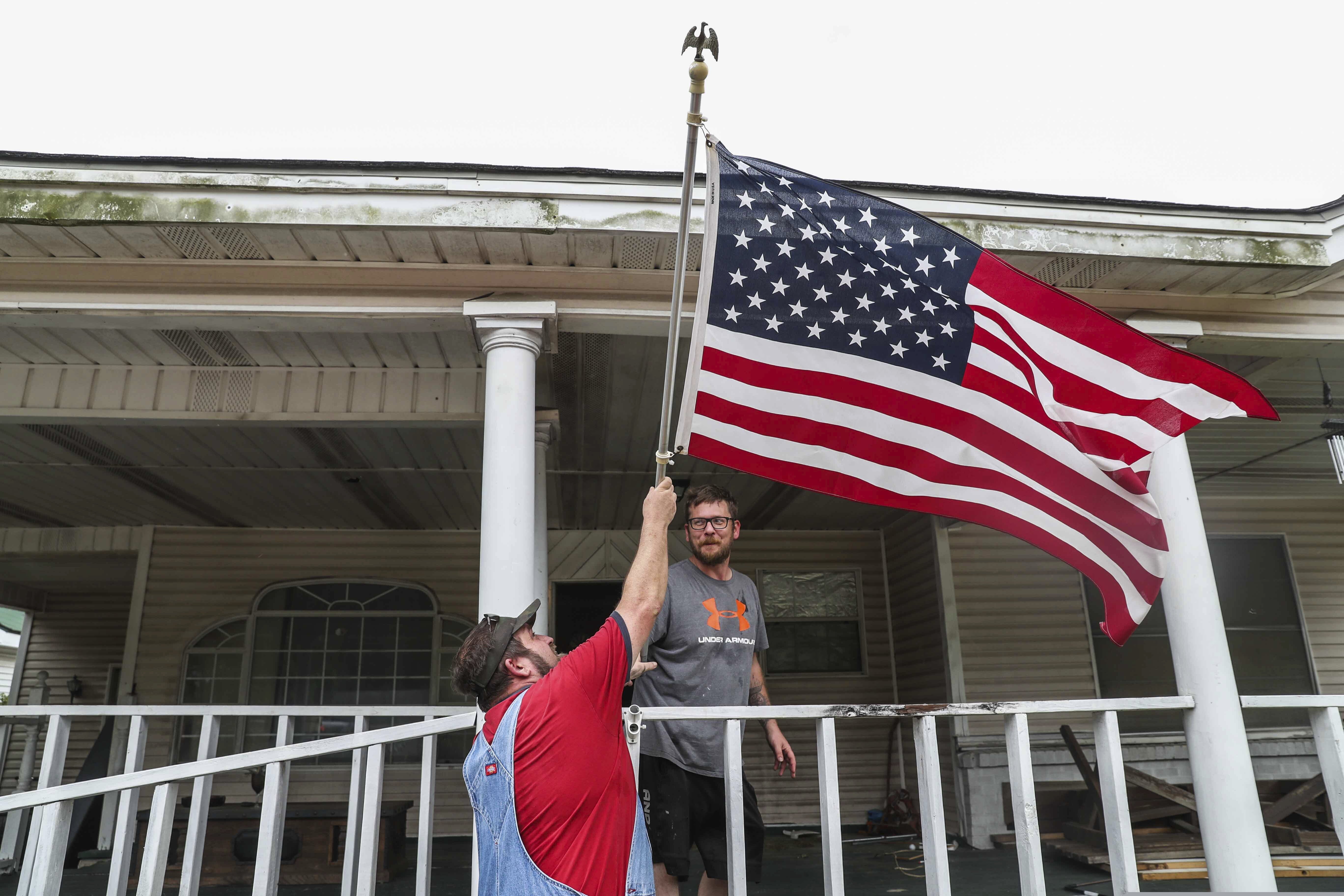 Bob Keen and Jonathan Trotti take down the American flag from their front porch to keep it safe inside the house while they prepare to evacuate the area as Hurricane Laura approaches in West Orange on Wednesday, August 26, 2020. (Lola Gomez/Austin American-Statesman via AP)