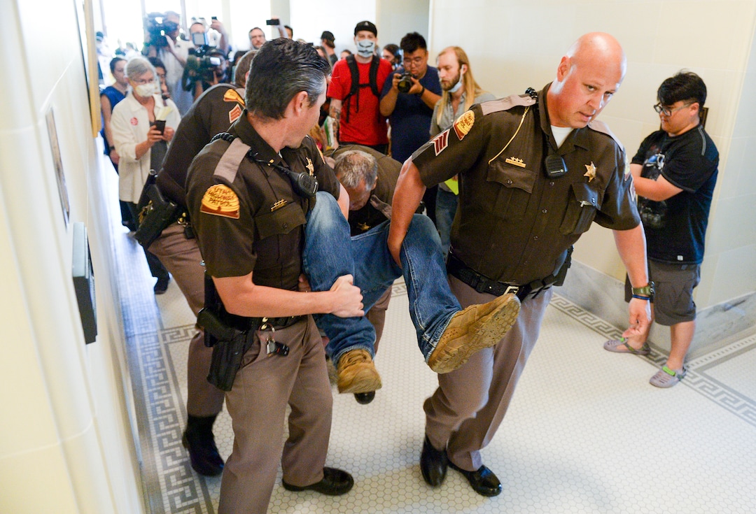 (Leah Hogsten  |  The Salt Lake Tribune) Ethan PetersenÊwithÊCivil Riot, a SLC-basedÊcivilÊresistance collective, and other opponents of the proposed inland port are escorted out of the Utah Inland Port Authority Board meeting by Utah Highway Patrol officers at the Capitol, June 5, 2019. The Inland Port Authority Board had to cancel its meeting last month after a group of protesters took over the meeting. Petersen was arrested.