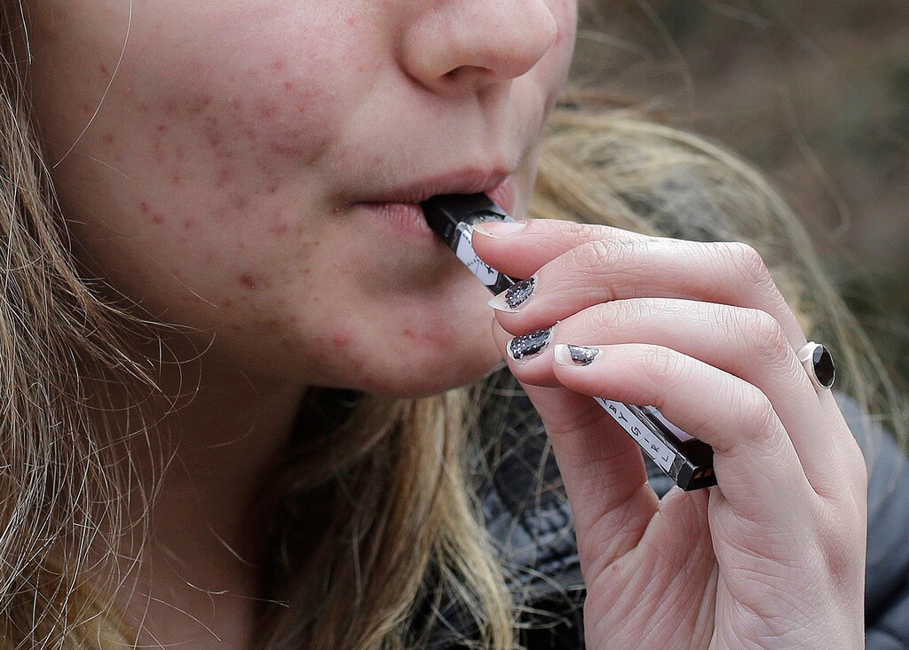 (Steven Senne | AP file photo) In this April 11, 2018, file photo, a high school student uses a vaping device near a school campus in Cambridge, Mass. The Trump administration announced Thursday that it will prohibit fruit, candy, mint and dessert flavors from small, cartridge-based e-cigarettes that are popular with high school students. But menthol and tobacco-flavored e-cigarettes will be allowed to remain on the market.