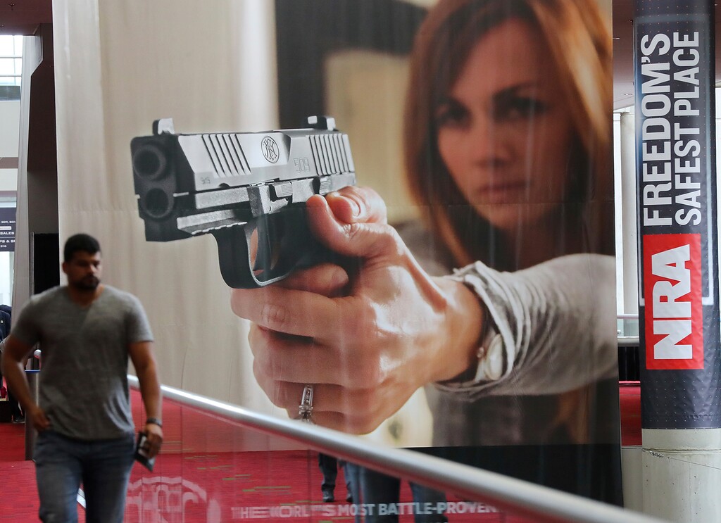 FILE - In this April 27, 2017, file photo, an attendee passes by a large banner advertising a handgun during the National Rifle Association convention at the Georgia World Congress Center in Atlanta. (Curtis Compton/Atlanta Journal-Constitution via AP, File)
