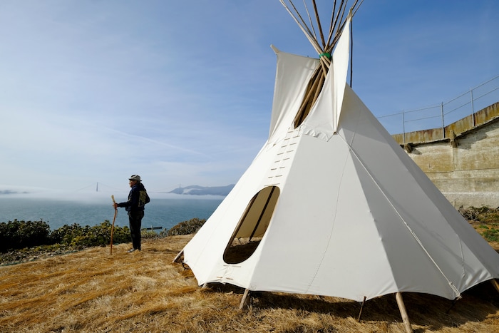 (Eric Risberg | AP) In this photo taken Tuesday, Nov. 12, 2019, Eloy Martinez, who took part in the Native American occupation of Alcatraz 50 years earlier, stands by a teepee on the island and looks out toward the bay and Golden Gate Bridge in San Francisco. The week of Nov. 18, 2019, marks 50 years since the beginning of a months-long Native American occupation at Alcatraz Island in the San Francisco Bay.