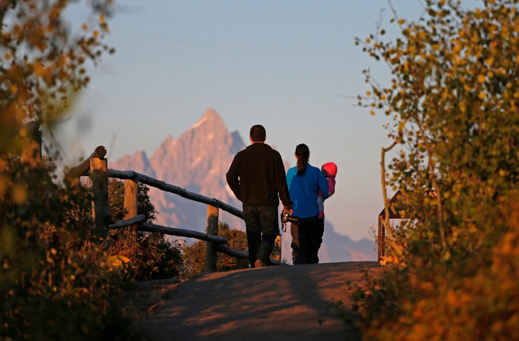 FILE - In this Aug 25, 2016 file photo, on the 100th anniversary of the National Park Service, visitors stroll with their baby as the sun at dawn illuminates mountain peaks as seen from Signal Mountain in Grand Teton National Park, Wyo. Visitation to America's national parks has set new records for three consecutive years. (AP Photo/Brennan Linsley, file)