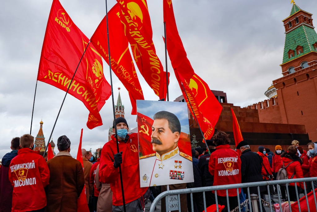A man holds a portrait of former Soviet leader Josef Stalin as other communist party supporters with red flags gather to lay flowers at the Vladimir Lenin Mausoleum marking the 103rd anniversary of the 1917 Bolshevik revolution on Red Square in Moscow, Russia, Saturday, Nov. 7, 2020. (AP Photo/Alexander Zemlianichenko)