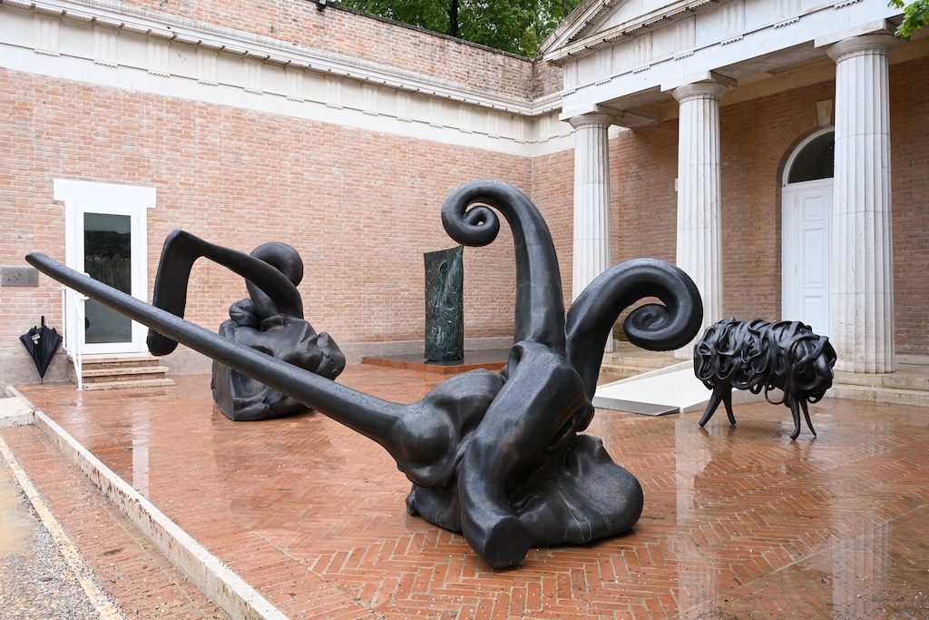 (Casey Kelbaugh | The New York Times) Two sparring bronze figures in foreground, 2024, and right, black sheep, 2026, part of American sculptor Alma Allen’s “Call Me the Breeze” presentation in the Giardini of the Venice Biennale in Venice, Italy, May 6, 2026.