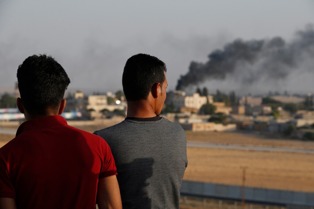 (Lefteris Pitarakis | AP) People standing on a rooftop in Akcakale, Sanliurfa province, southeastern Turkey, at the border with Syria, watch as in the background smoke billows from fires caused by Turkish bombardment in Tal Abyad, Syria, on Sunday, Oct. 13, 2019. Turkey's official Anadolu news agency says Turkey-backed Syrian forces have advanced into the center of a Syrian border town, Tal Abyad, on the fifth day of the Turkey's military offensive against Kurdish fighters in Syria.