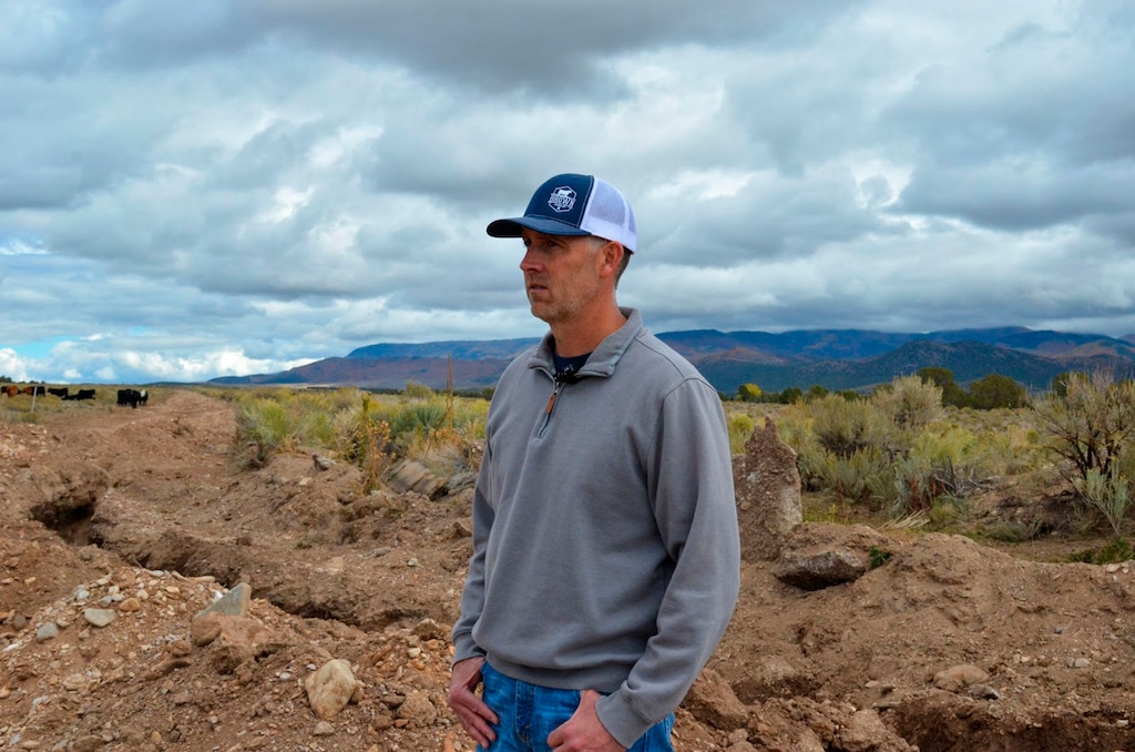 (Lexi Peery | KUER-FM via AP) Trent Brown, a long-time farmer and rancher in Beaver County, stands next to a ditch that brings water from a nearby reservoir to his farm and others nearby Wednesday Oct. 6, 2021, in Beaver County, Utah. He used a grant from the state's Water Optimization Program to replace the cement in the ditch earlier this year, making it more efficient.