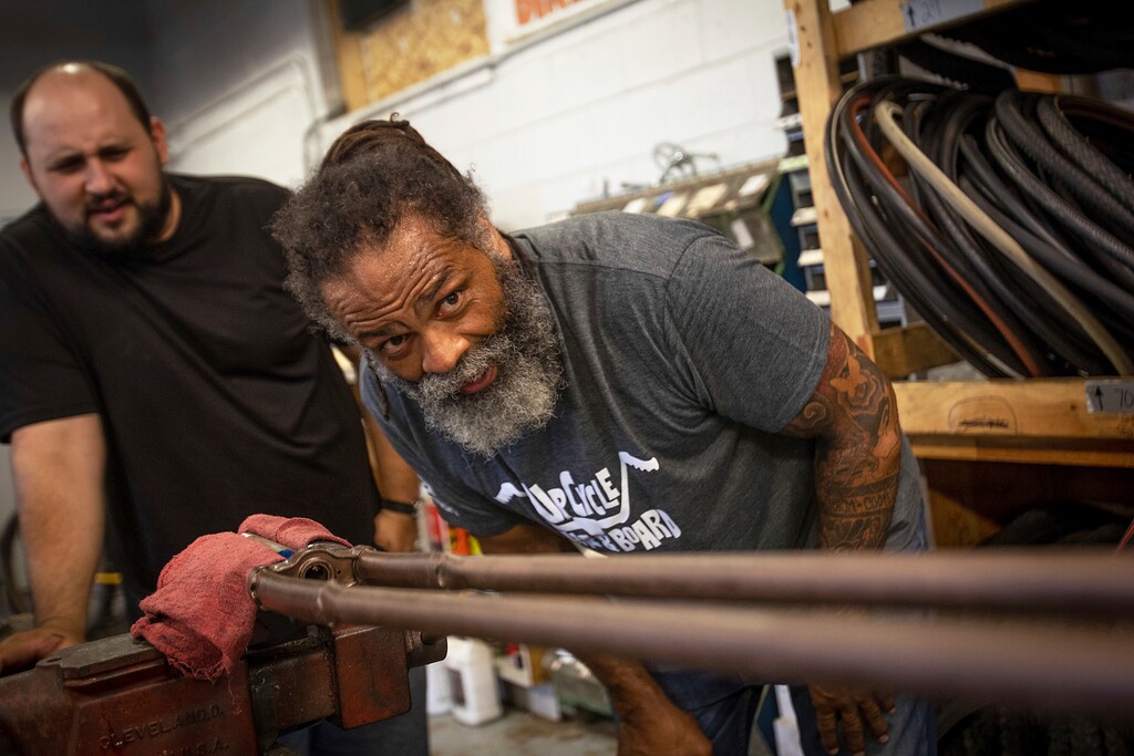 (Benjamin Zack | Standard-Examiner | The Associated Press) In this Tuesday, Aug. 7, 2018 photo, Mark Johnson, right, and J.P. Orquiz work on the giant forks from one of Johnson's homemade bikes at the Ogden Bicycle Collective in Ogden, Utah. Johnson is starting a business that rebuilds old bikes and scraps into rideable pieces of art. "I want to ride a bike that's kind of dangerous, that's a little sketchy, that's a little scary," said Johnson.