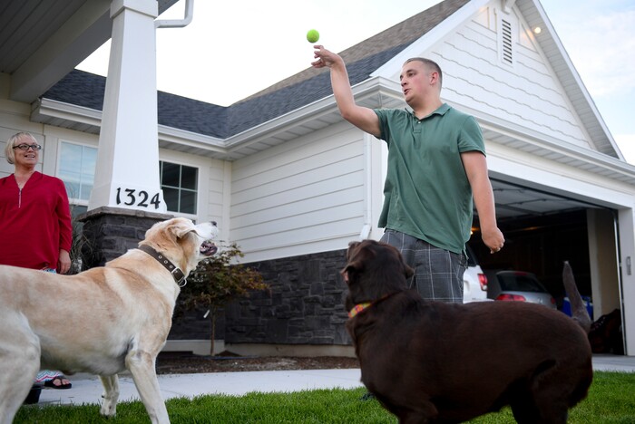 ADVANCE FOR WEEKEND EDITIONS - In this Aug. 16, 2017, photo, Gage Bowls plays fetch with his dogs Buster, left, and Bentley as his mother, Jodi Bowls, watches outside of the Bowls' home in Spanish Fork, Utah. At birth, Gage suffered four hours of oxygen depravation which left him with mental and physical deficiencies, including cerebral palsy. (Isaac Hale/The Daily Herald via AP)