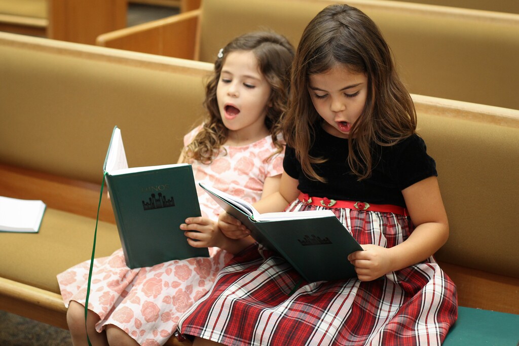 (The Church of Jesus Christ of Latter-day Saints) Two girls sing from a Latter-day Saint hymnbook. A scholar notes that the beloved hymn "Love at Home" traces its roots back to 19th-century "blackface minstrelsy."