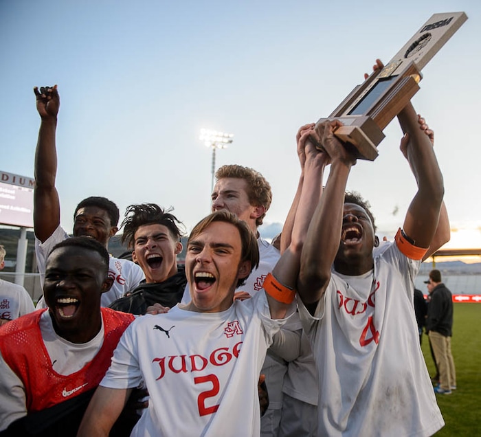 (Trent Nelson | The Salt Lake Tribune)  Judge Memorial players celebrate their win over Morgan High School in the 3A state championship game, Saturday May 12, 2018. Holding the trophy is Ferdinand Bambabate.
