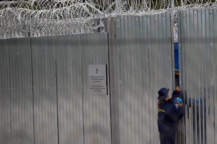 A member of the armed security guards opens the gate of a heavily guarded camp at Serbia's border with Hungary, near the Horgos border crossing, Serbia, Tuesday, Sept. 19, 2017. The European Union border that saw hundreds of thousands of migrants enter freely in 2015 has since become a sealed fortress with two rows of fence and closed border camps that the United Nations have described as “in effect detention centers.” (AP Photo/Darko Vojinovic)